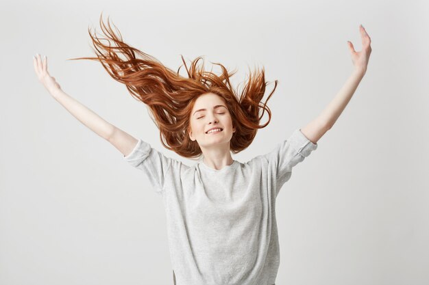 Ritratto di giovane ragazza allegra bella rossa sorridente con gli occhi chiusi, agitando i capelli.