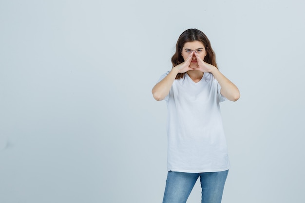 Ritratto di giovane ragazza che tiene le mani per dire il segreto in t-shirt bianca, jeans e vista frontale seria