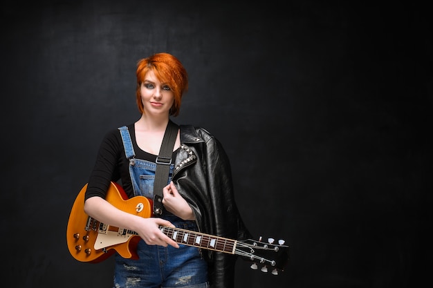 Ritratto di giovane ragazza con la chitarra su sfondo nero.