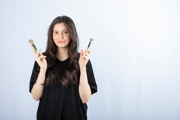 Ritratto di giovane ragazza con spazzole cosmetiche che guarda l'obbiettivo su bianco.