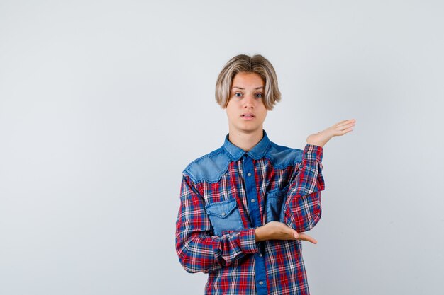 Ritratto di giovane ragazzo adolescente che finge di tenere qualcosa in una camicia a quadri e sembra una vista frontale perplessa