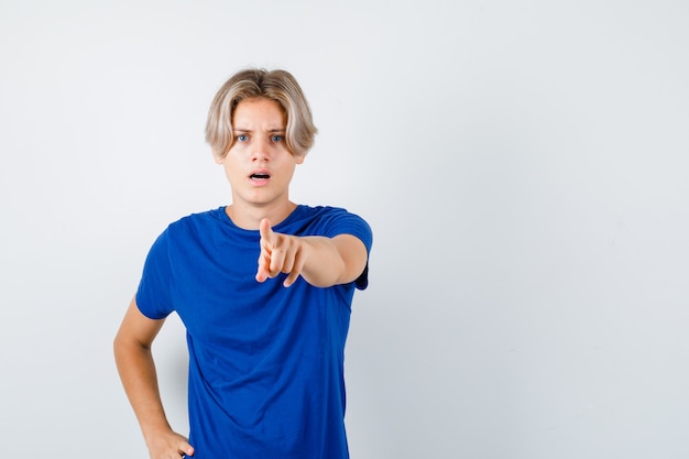 Ritratto di giovane ragazzo adolescente che punta in avanti in maglietta blu e guarda perplesso vista frontale