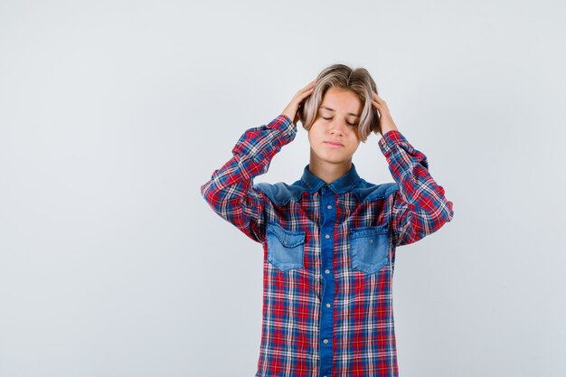 Ritratto di giovane ragazzo adolescente con le mani sulla testa in camicia a quadri e guardando esausto vista frontale