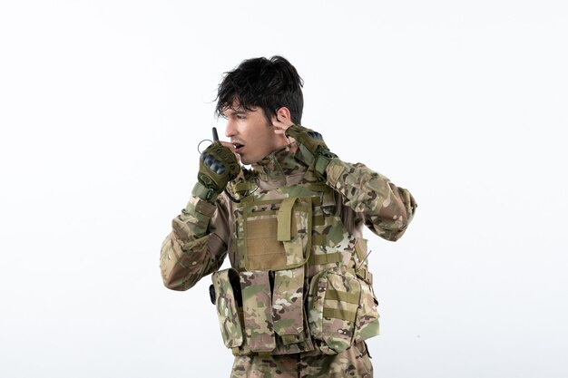 Ritratto di giovane soldato in mimetica che parla attraverso il muro bianco del walkie-talkie