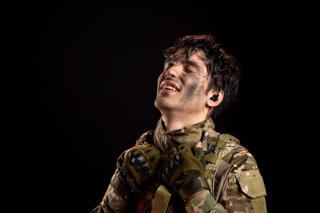 Ritratto di giovane soldato sollevato in uniforme sul muro scuro