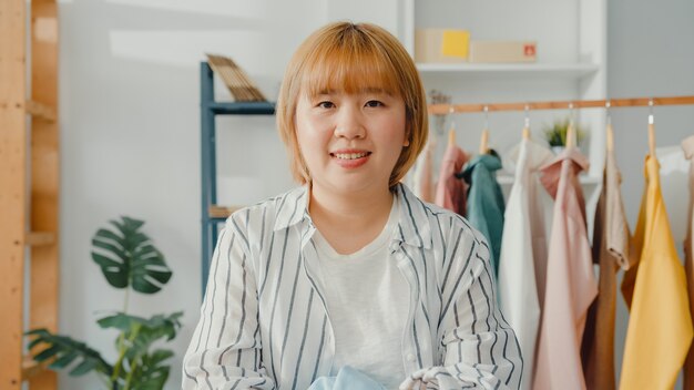 Ritratto di giovane stilista di moda signora asiatica con sorriso felice, braccia incrociate e guardando davanti mentre lavorava nel negozio di abbigliamento in ufficio a casa