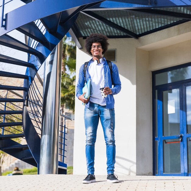 Ritratto di giovane studente maschio afro che sta davanti all&#39;edificio universitario