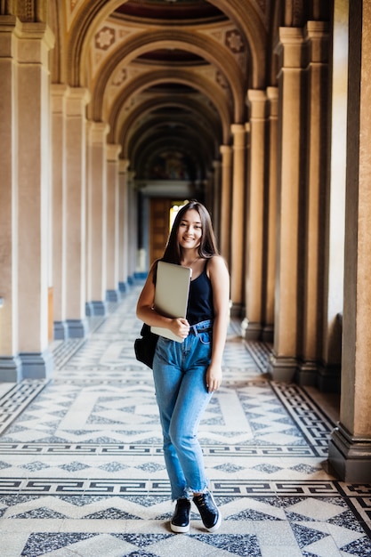 Ritratto di giovane studentessa asiatica che utilizza un computer portatile o un tablet in posa intelligente e felice all'università o al college,