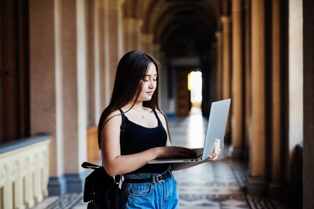 Ritratto di giovane studentessa asiatica che utilizza un computer portatile o un tablet in posa intelligente e felice all'università o al college,