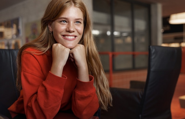 Ritratto di giovane studentessa attraente rossa, si siede su una poltrona appoggiata sulle braccia e sorridente.