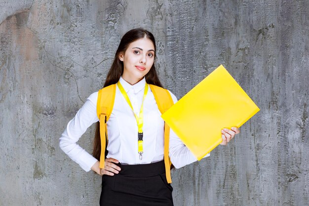 Ritratto di giovane studentessa con taccuino giallo in piedi sopra il grigio. Foto di alta qualità