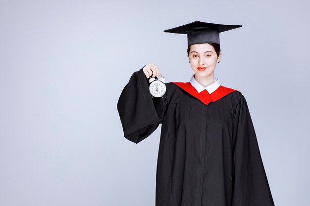 Ritratto di giovane studentessa laureata che tiene l'orologio per mostrare il tempo. Foto di alta qualità