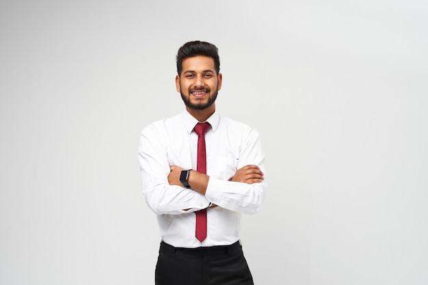 Ritratto di giovane top manager indiano in maglietta e cravatta con le braccia incrociate e sorridente sul muro bianco isolato