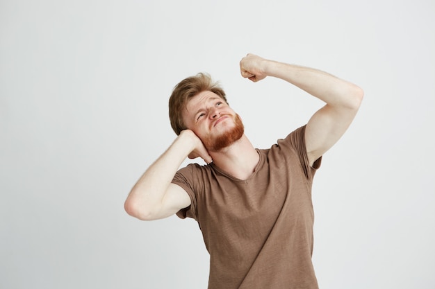 Ritratto di giovane uomo arrabbiato con le orecchie di chiusura della barba che osservano in su mostrando pugno.