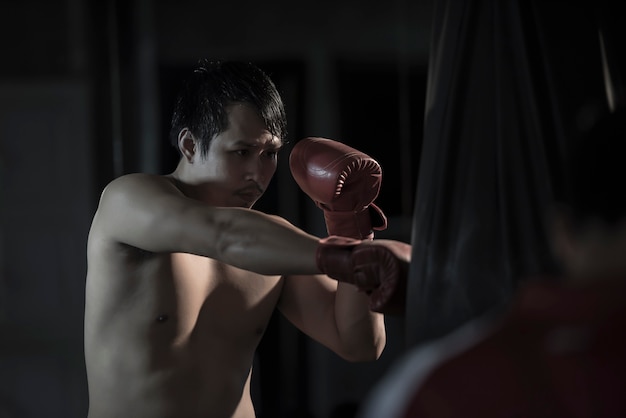 Ritratto di giovane uomo asiatico che pratica pugilato su un punching ball alla palestra.