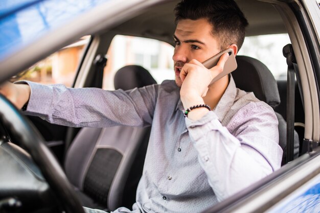 Ritratto di giovane uomo bello che conduce automobile e che parla sul telefono cellulare.