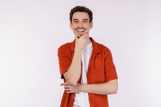 Ritratto di giovane uomo bello che guarda fiducioso verso la telecamera con un sorriso con le braccia incrociate e la mano alzata sul mento su sfondo isolato