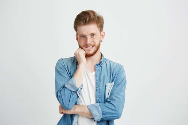 Ritratto di giovane uomo bello emotivo che pensa con la mano sul labbro mordace del mento.