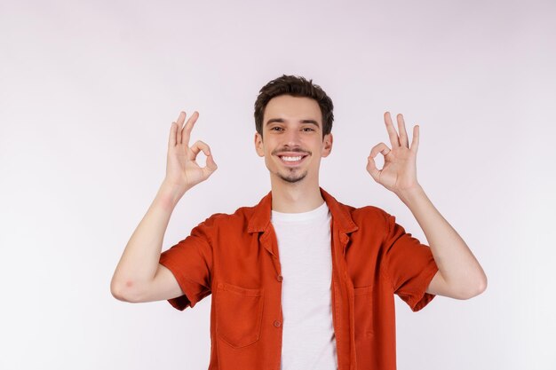 Ritratto di giovane uomo bello felice che fa segno giusto con la mano e le dita su sfondo bianco