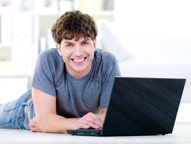 Ritratto di giovane uomo bello felice con il portatile - al chiuso