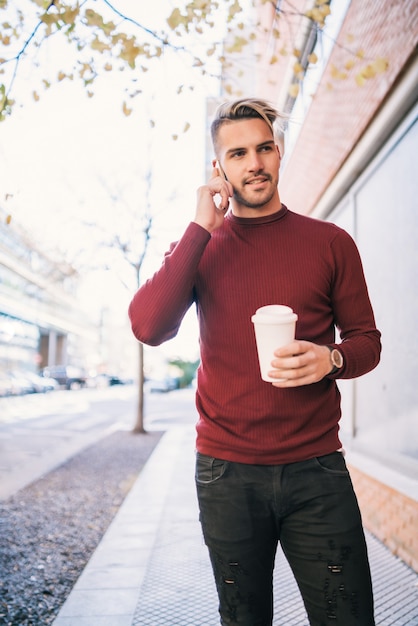 Ritratto di giovane uomo bello parlare al telefono mentre si tiene una tazza di caffè all'aperto in strada. Concetto di comunicazione.