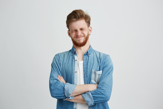 Ritratto di giovane uomo bello scontento in camicia di jeans con le braccia incrociate.