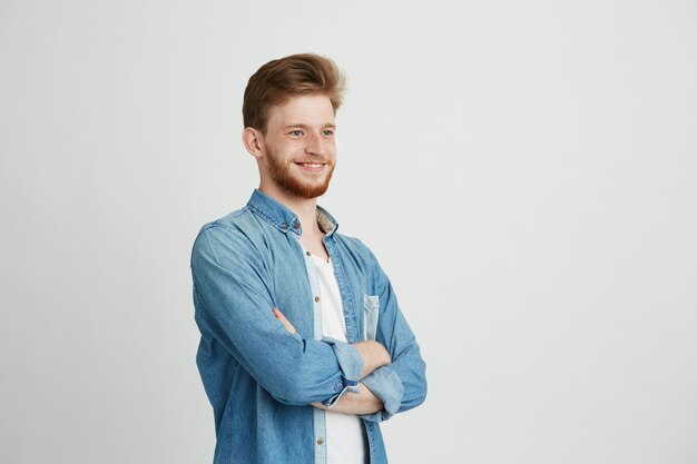 Ritratto di giovane uomo bello sicuro allegro con sorridere della barba. Braccia incrociate.