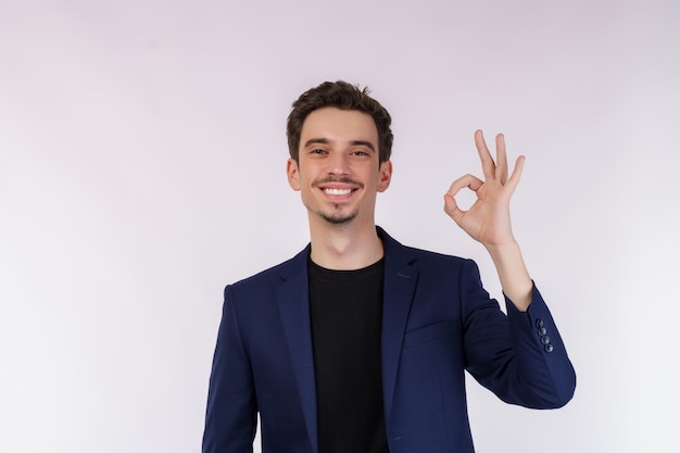 Ritratto di giovane uomo d'affari bello felice che fa segno giusto con la mano e le dita su sfondo bianco