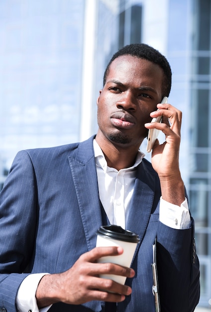 Ritratto di giovane uomo d&#39;affari che parla sul telefono cellulare che tiene la tazza di caffè eliminabile