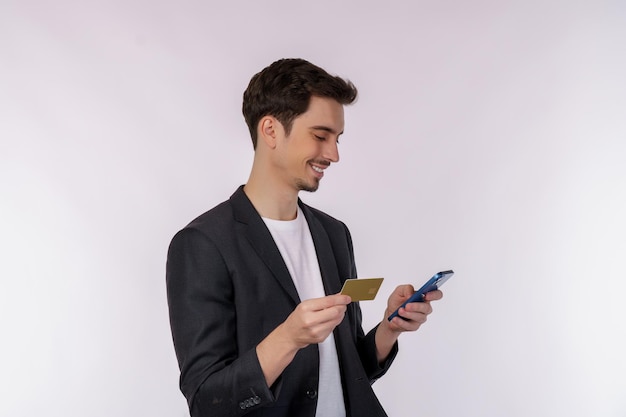 Ritratto di giovane uomo d'affari felice in piedi utilizzando il telefono cellulare e tenendo la carta di credito isolato su sfondo bianco colore studio