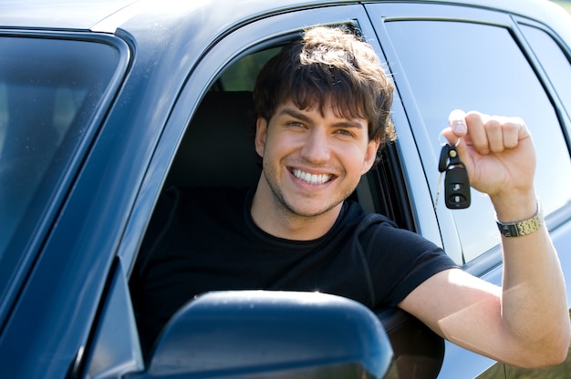 Ritratto di giovane uomo felice di successo che mostra le chiavi che si siedono nella nuova automobile