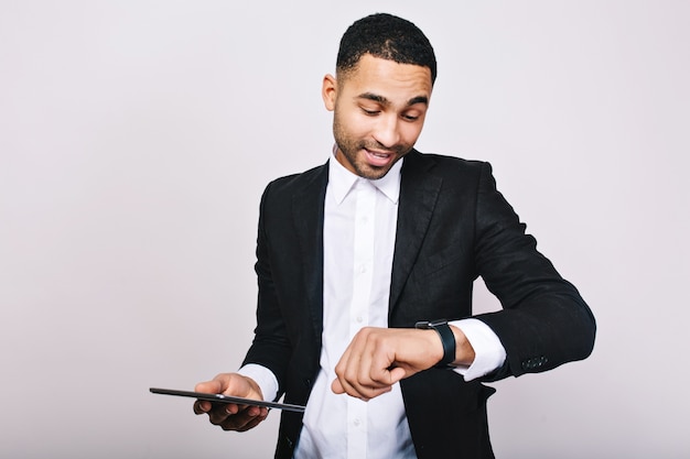 Ritratto di giovane uomo impegnato di successo in camicia bianca, giacca nera, con tablet guardando l'orologio. Elegante uomo d'affari, essere impegnato, tempo per il lavoro, riunioni, leadership.