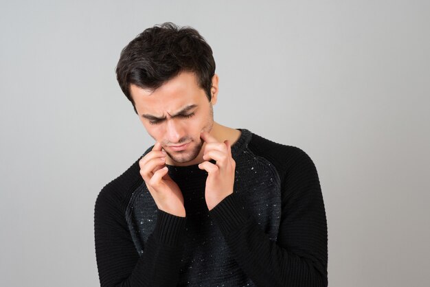 Ritratto di giovane uomo in abiti casual che guarda al ribasso sul muro grigio