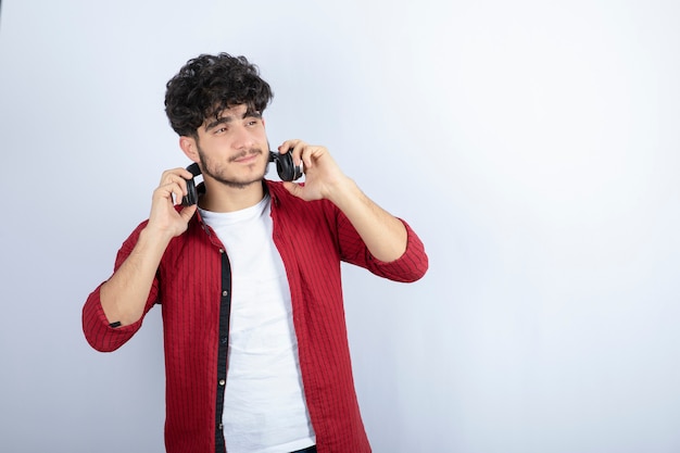 Ritratto di giovane uomo in cuffie ascoltando la canzone sul muro bianco.