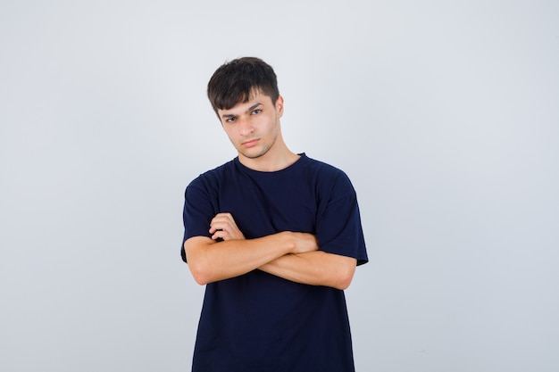 Ritratto di giovane uomo in piedi con le braccia incrociate in maglietta nera e guardando grave vista frontale