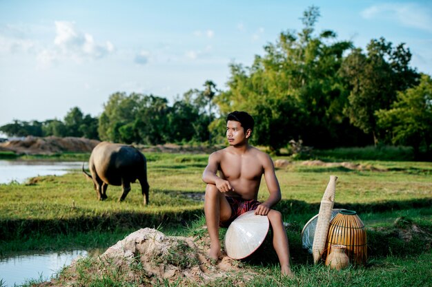 Ritratto di giovane uomo in topless che indossa perizoma in stile di vita rurale seduto con trappola di pesca in bambù