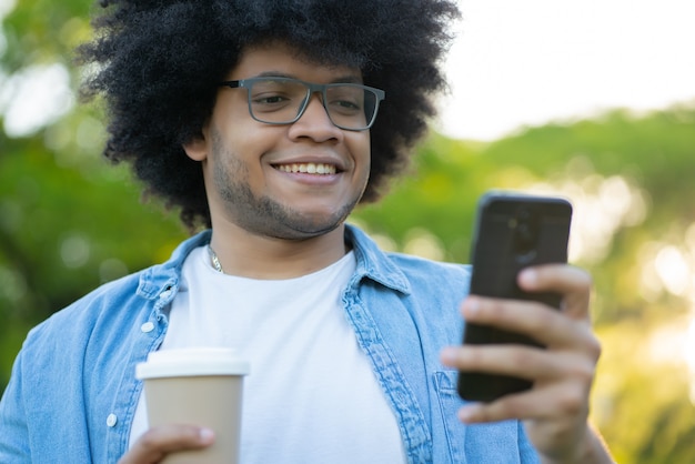 Ritratto di giovane uomo latino utilizzando il suo telefono cellulare in piedi all'aperto sulla strada