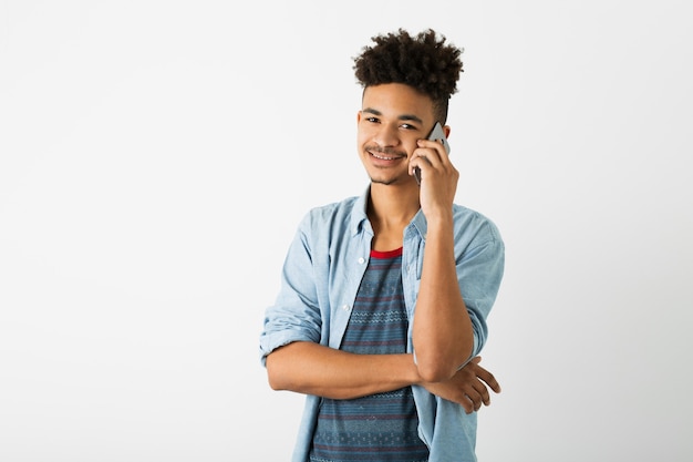 Ritratto di giovane uomo nero hipster in posa sul fondo bianco isolato della parete dello studio, vestito elegante, acconciatura afro divertente, sorridente, felice, parlando al telefono intelligente, guardando nella fotocamera