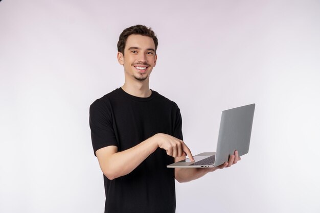 Ritratto di giovane uomo sorridente bello che tiene il computer portatile in mano digitando e sfogliando pagine web isolate su sfondo bianco