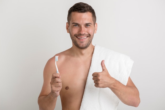 Ritratto di giovane uomo sorridente che mostra pollice sul gesto mentre si tiene lo spazzolino da denti