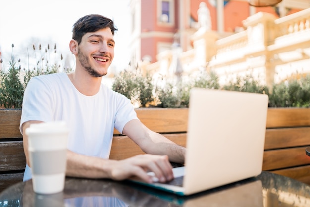 Ritratto di giovane uomo utilizzando il suo computer portatile mentre è seduto in una caffetteria. Concetto di tecnologia e stile di vita.