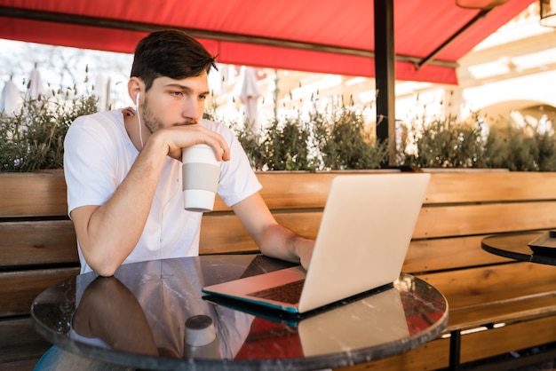 Ritratto di giovane uomo utilizzando il suo computer portatile mentre è seduto in una caffetteria. Concetto di tecnologia e stile di vita.