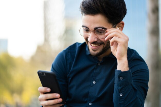 Ritratto di giovane uomo utilizzando il suo telefono cellulare mentre è seduto su una panchina all'aperto. Concetto urbano.