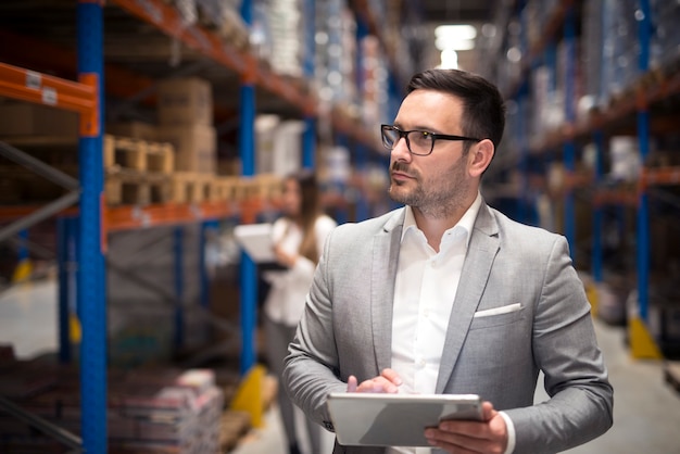 Ritratto di imprenditore di successo manager CEO tenendo tablet e camminando attraverso l'area di stoccaggio del magazzino guardando verso gli scaffali