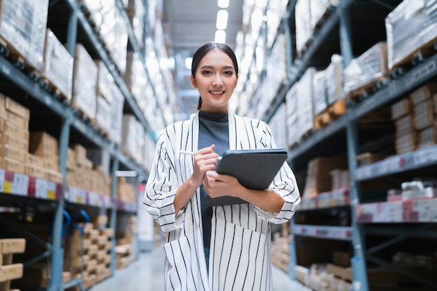 Ritratto di imprenditore donna asiatica che utilizza tablet digitale che controlla la quantità di inventario di prodotti in stock sullo scaffale del magazzino di distribuzione factorylogistic servizio di spedizione e consegna