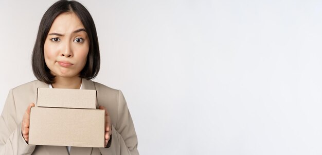 Ritratto di imprenditore femminile asiatico commessa in possesso di scatole e guardando triste deluso in piedi su sfondo bianco