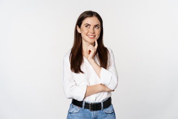 Ritratto di imprenditore femminile che pensa, fa la scelta, in piedi premuroso, sfondo bianco dello studio.