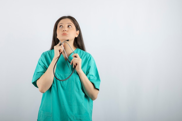 Ritratto di infermiera femminile con stetoscopio guardando da qualche parte su bianco.