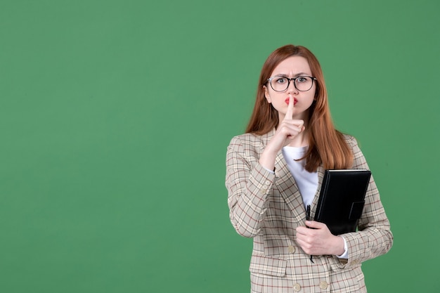 Ritratto di insegnante femminile con blocco note che chiede di tacere sul verde