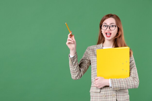 Ritratto di insegnante femminile in posa con file giallo e matita felice su green